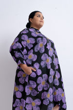 Loose-fitting dress with purple and yellow floral pattern, long sleeves, against white wall.