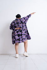 Dynamic back view of Para Dress with large purple and pink floral pattern, hair tied back, and white shoes.