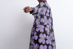 Side view of person in floral Para Dress, arm extended forward, large purple daisy flowers, head not shown.