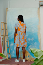 Back view of a person in Helia Dress with orange circular pattern, facing a canvas in a white-walled artist’s studio.