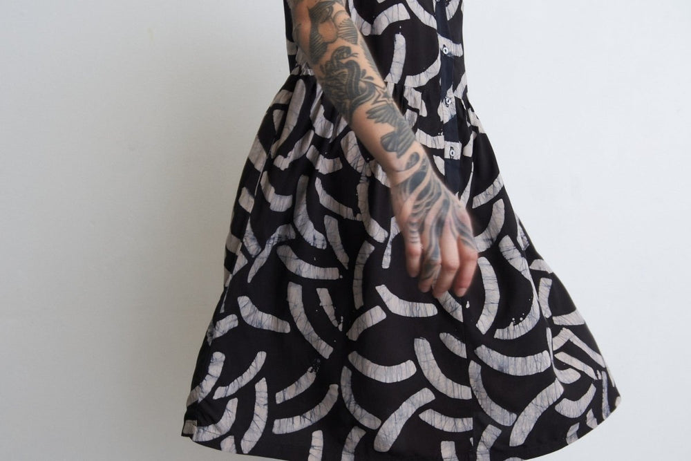 Helia Dress in Cantaloop print, arm tattoo detail, against a minimalist backdrop, exuding modern chic.