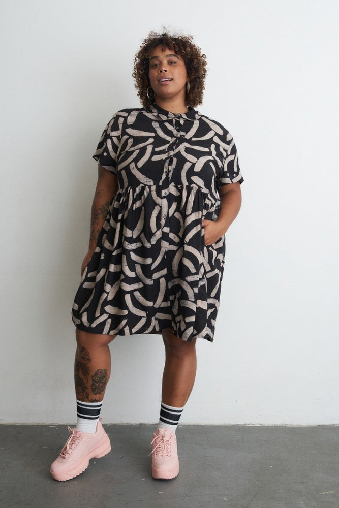 Helia Dress in Cantaloop print against white backdrop, tattoos and striped socks with pink sneakers.