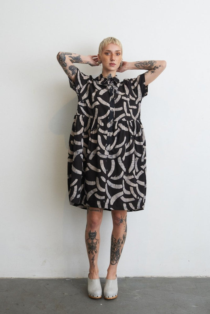 Helia Dress in Cantaloop print against white wall, tattoos and white shoes enhancing the bold print.