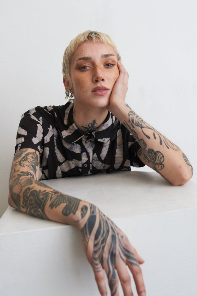Person in Helia Dress with intricate arm tattoos against a plain white backdrop, exuding artistic flair.