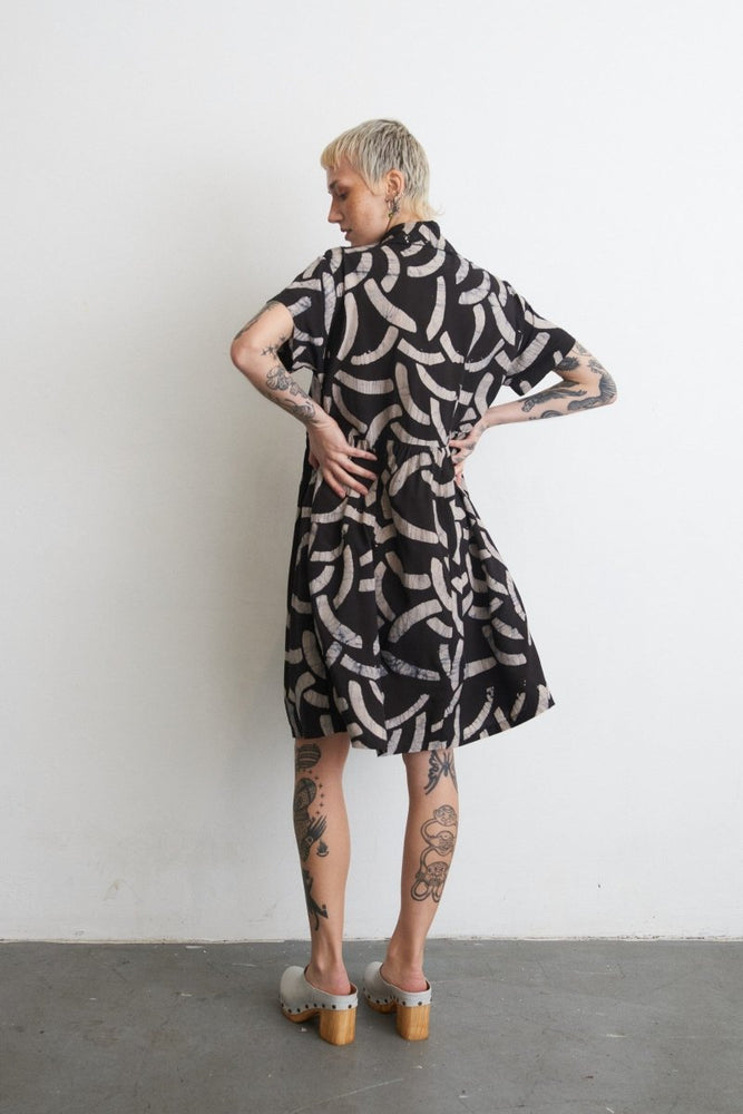 Helia Dress in Cantaloop print against white wall, tattoos and grey shoes complementing the look.