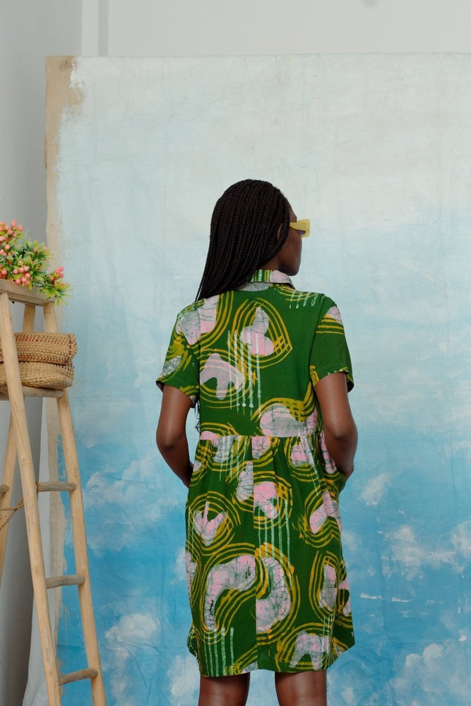 Back view of Helia Dress in Waters print, long braided hair, standing before canvas, with floral ladder.