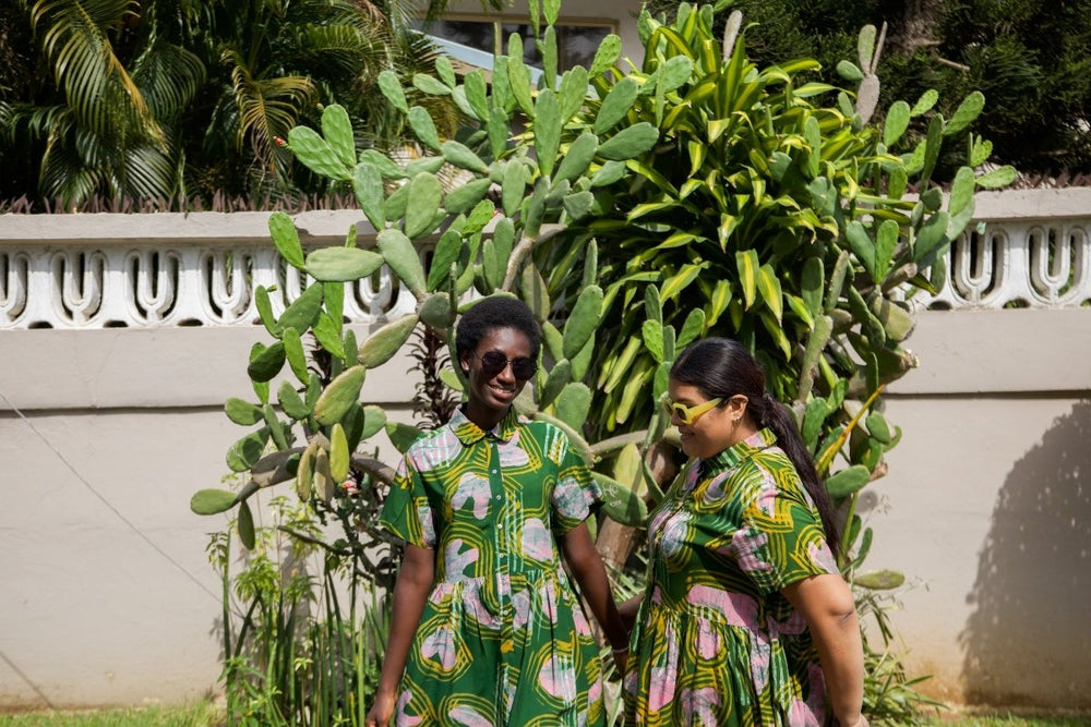 Two women wear the Helia Dress in Waters print, paired with cactus backdrop, showcasing green patterned design.