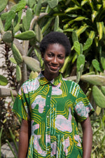 Model stands outdoors in the Helia Dress against cactus backdrop, the dress has a green-yellow and pink print.