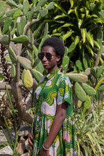 Helia Dress in Waters print, model wears sunglasses, amidst greenery with cacti and succulents backdrop.