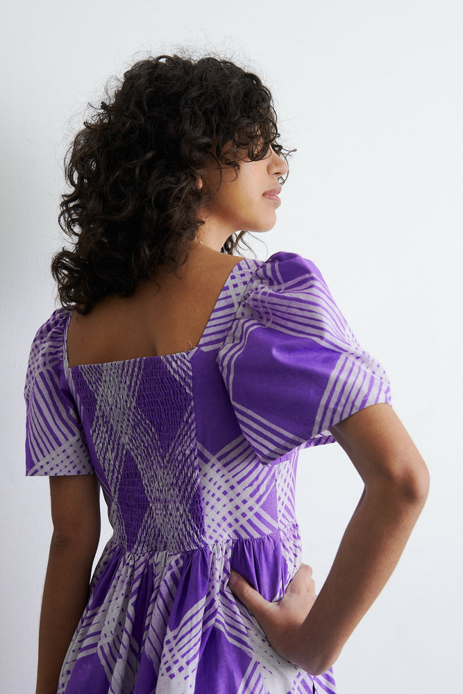 Back view of a purple & white Abeo dress. Hand dyed 100% cotton, puffed sleeves, rouching at back, full skirt, pockets!