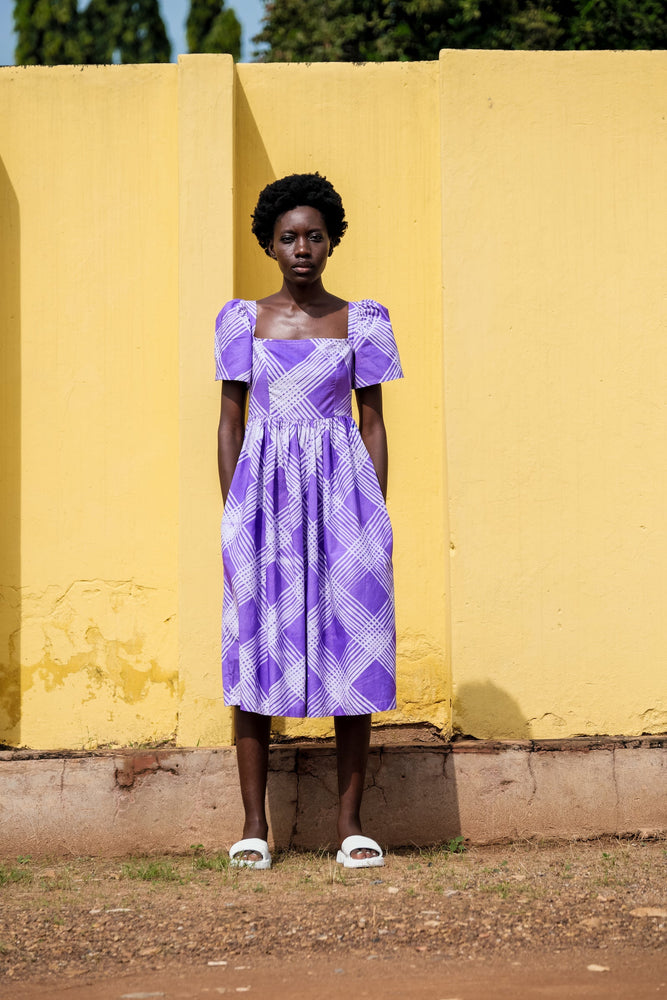 Stylish woman in purple dress against yellow wall. Hand dyed cotton dress with puffed sleeves, rouching at back, and pockets!