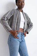 Woman in jeans and jacket against wall. Abiba Jacket: handwoven cotton. Loose-fitting blazer style with inside pocket.
