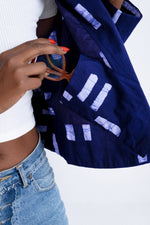 Midsection view of trendy Abiba Jacket with sunglasses, showcasing hand-dyed pattern and denim pairing, on white background.