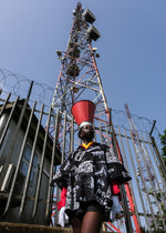 Person in Album Garment with welding mask, standing before a red and white communication tower.