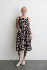 Sleeveless Amplo Dress in abstract pattern, mid-calf length, accentuated with tattoos and stylish white clog shoes.