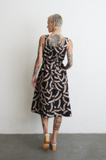 Back view of Amplo Dress in an abstract black & beige batik print, highlighting intricate tattoos and chic white clogs.