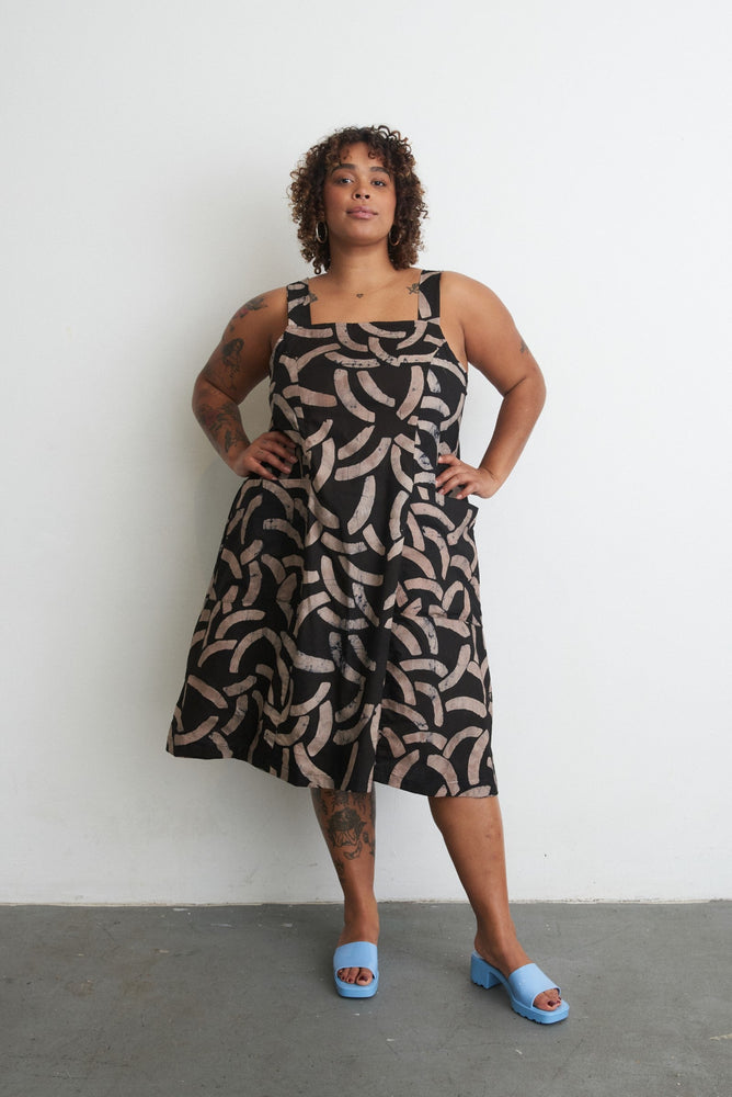 Confident stance in Amplo Dress with dark leafy pattern, sleeveless design, and tattoos complementing the look.