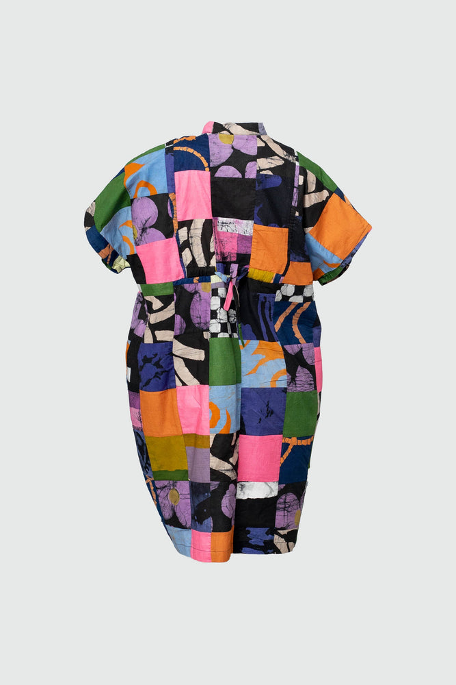 Back view of vibrant Bata Dress in Motley, short-sleeved with colorful patchwork, displayed against a light, plain backdrop.