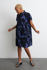 Chic Bata Dress with abstract blueish-purple print, short sleeves, and knee-length cut, against a white backdrop.