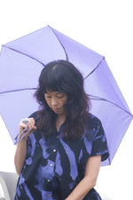 Contemporary Bata Dress, purple umbrella accessory, mysterious foggy field ambiance.