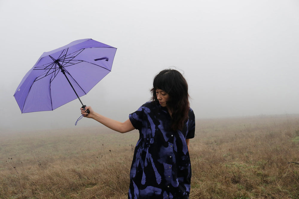 Abstract Bata Dress with purple umbrella, moody field backdrop, and unique blue-black print.