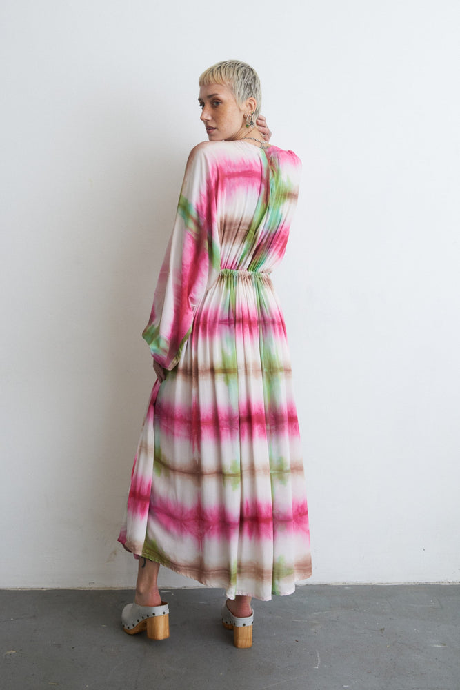 Serene Dreams Bata Dress with pink and green tie-dye, cinched waist, and grey clogs, against a white wall.