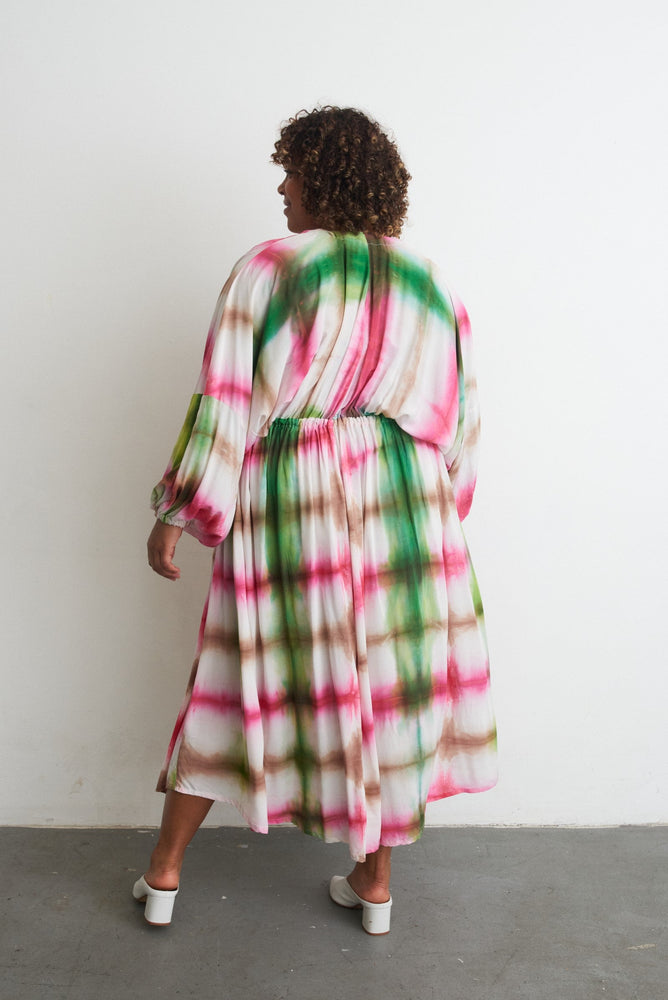 Serene Dreams Bata Dress with a colorful tie-dye pattern, long sleeves, and white heels, against a white wall.