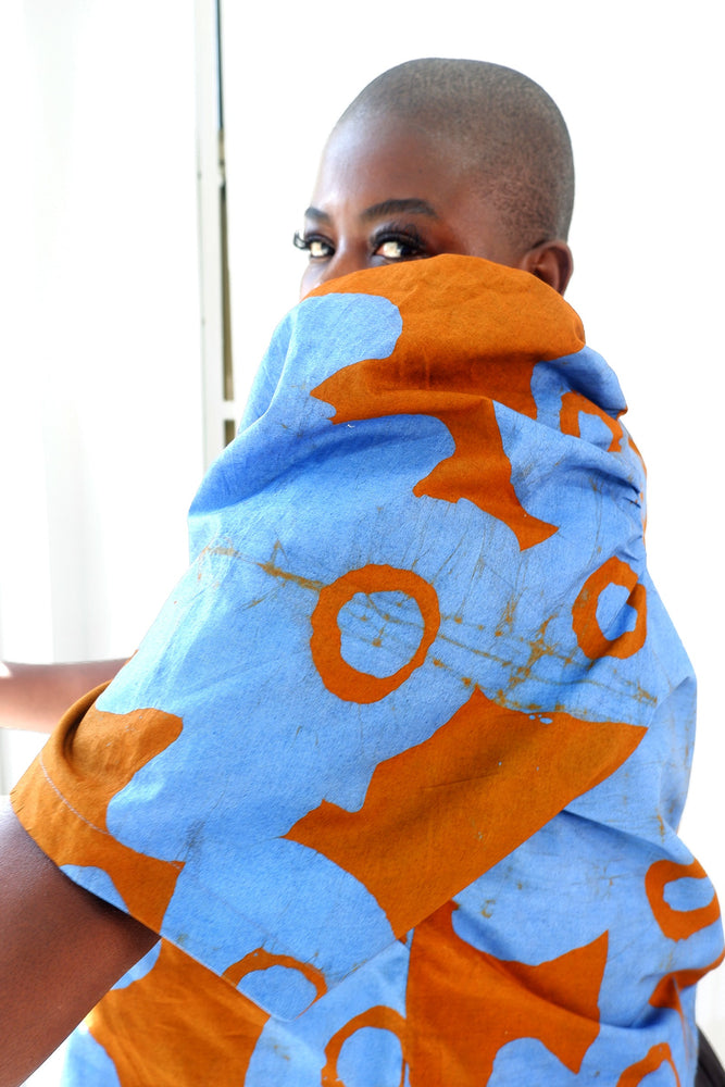 Woman in vibrant blue and orange garment, abstract patterns, light fabric, Her face hidden behind the puffed sleeve.
