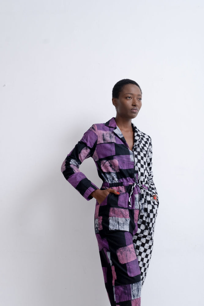 Accra Jumpsuit in Adepa, featuring purple and black patchwork and checkered patterns, cinched at the waist, white backdrop.