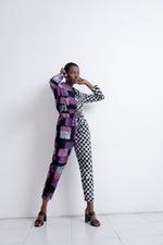 Accra Jumpsuit in Adepa print, split pattern with purple patchwork and checkered design, paired with dark strappy sandals.
