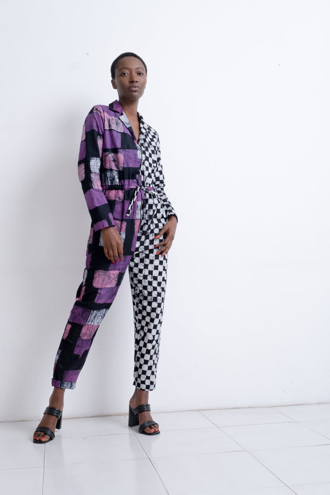 Unique Accra Jumpsuit in Adepa print, contrasting purple and checkered patterns, against a white backdrop with dark sandals.