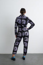 Rear view of Accra Jumpsuit in Good Signal print, highlighting drawstring waist and tapered legs, against a white wall.