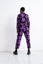 Back view of Love Perfect floral Accra jumpsuit, highlighting bold purple flowers on dark fabric, paired with black boots.