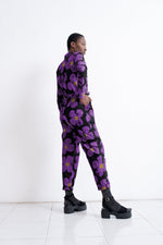 Love Perfect Accra jumpsuit in motion, purple blooms on dark, paired with chunky black shoes, white minimalist setting.