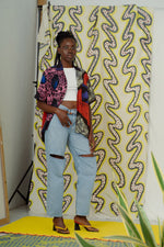 A woman in a colorful holiday shirt and jeans standing in front of a wall.