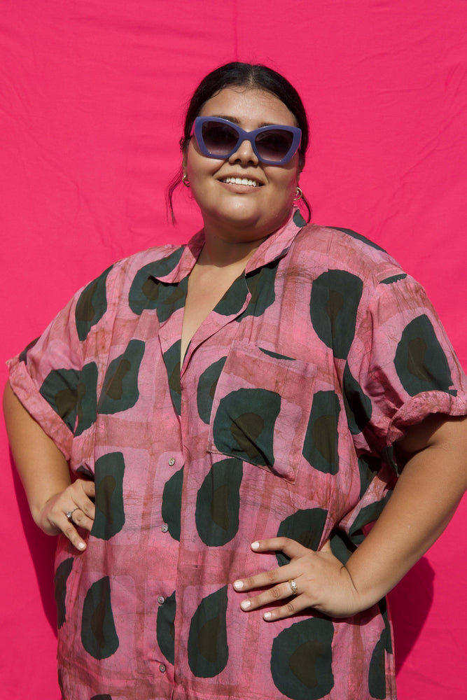 A happy woman wearing a rayon top with a vibrant pink and green batik print in a size 3.