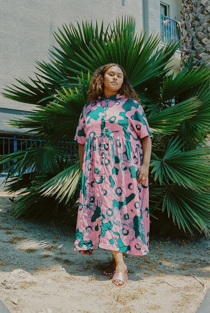 Imperium Dress in Pool Party print, with a pink base and green abstract patterns, set against a tropical backdrop.