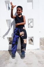 Cheerful child in Kids Tendo Pants, making a peace sign, in playful outdoor setting, crafted in Ghana.