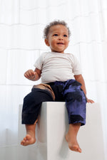 Playful toddler in durable Kids Tendo Pants, white tee, enjoying indoor fun, easy-to-wear with elastic waist.