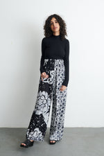 Latus Trousers in 2 Party System print, paired with a sleek black top, showcasing the bold prints and wide-leg style.