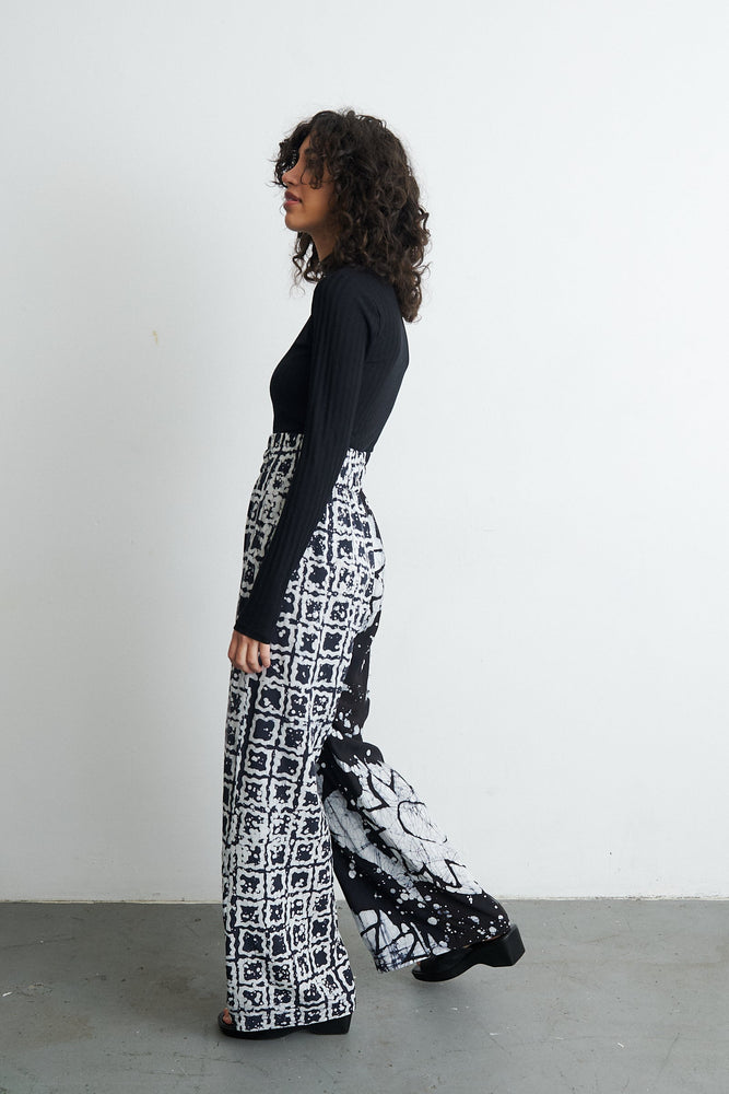 Chic Latus Trousers with 2 Party System print against a white wall, showcasing the abstract black and white design.