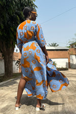 A woman wearing a vibrant orange and blue print dress called 'Letsa Wrap Dress in All Ideas.' The rayon fabric flowing.
