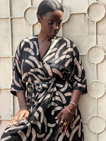 Woman in the Letsa dress in Cantaloop print with batwing sleeves, deep V neckline, and side slits, leaning against a wall.