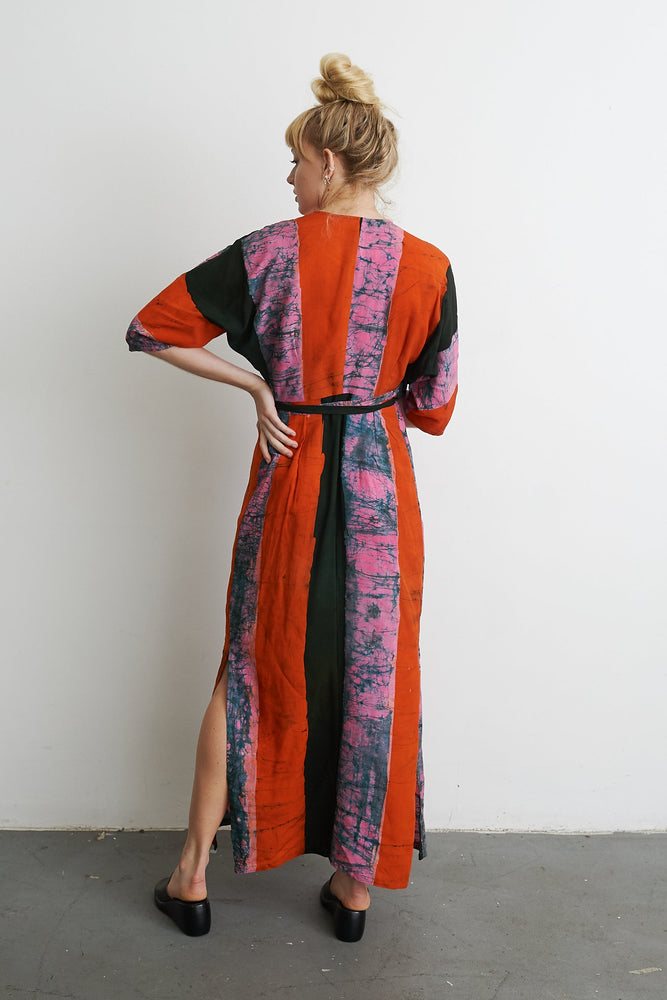 Woman in the Letsa Dress with Carmine print, back view, showcasing wide sleeves and cinched waist against a white wall.