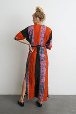 Woman in the Letsa Dress with Carmine print, back view, showcasing wide sleeves and cinched waist against a white wall.