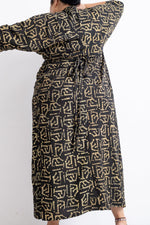 Back view of Letsa dress with long sleeves and golden abstract print, highlighting the waist tie and elegant drape.
