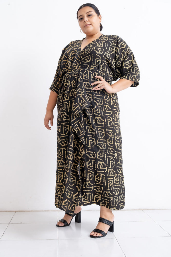 Letsa wrap dress with black and gold geometric design, showcasing drape and fit, paired with black open-toed heels.
