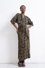 Letsa dress with black and gold geometric print, cinched waist with tie, batwing sleeves, paired with dark strappy sandals.
