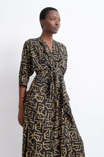 Flowing Letsa dress with intricate gold print on dark fabric, tied waist, and three-quarter sleeves against a white backdrop.