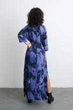 Rear view of Letsa Rorschach dress with abstract blueish purple and black print, curly hair, and black boots on grey floor.